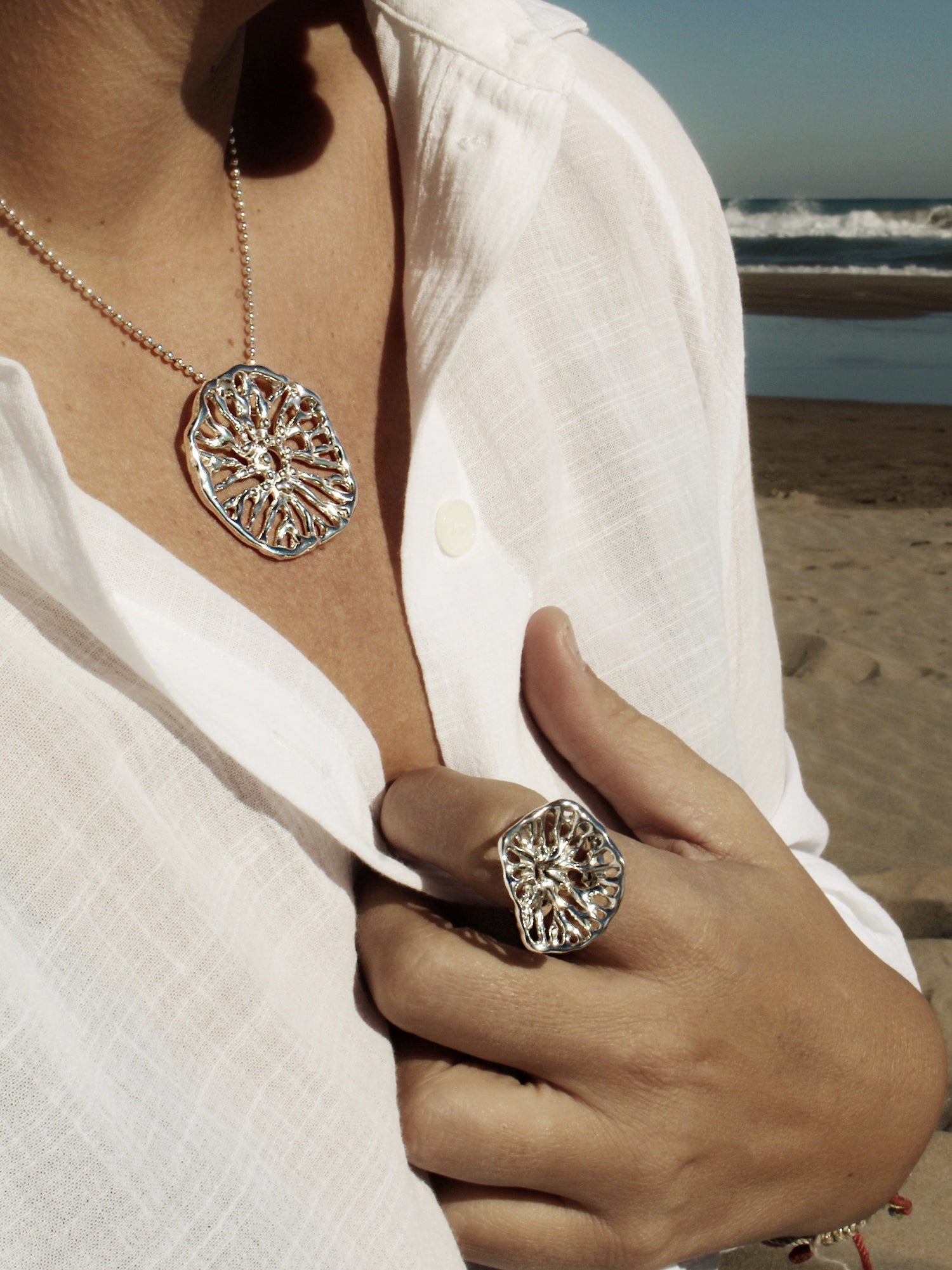 Person wearing a silver necklace and ring on a beach Flow Collection Naturalesa Jewelry