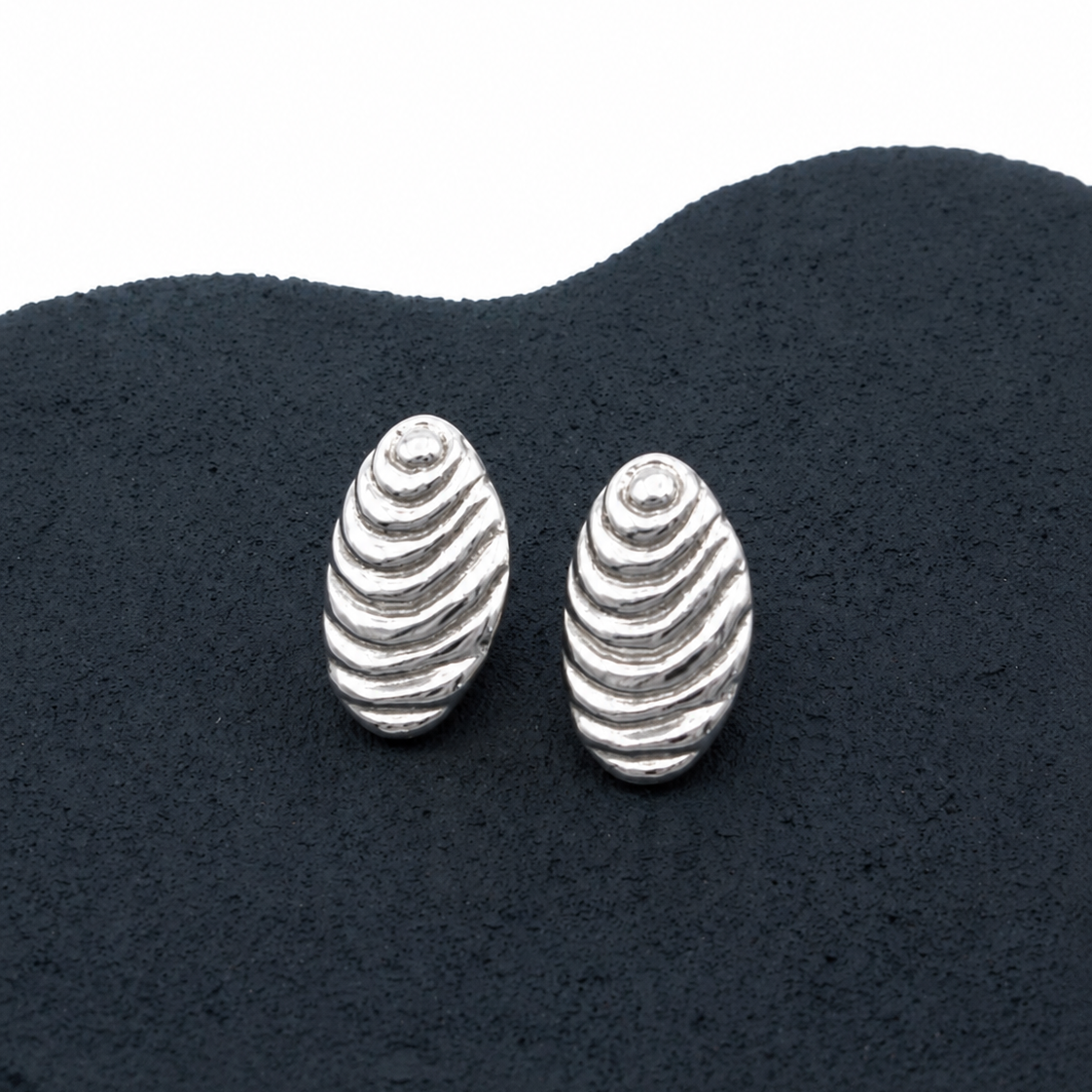 Silver shell-shaped earrings on a dark textured surface