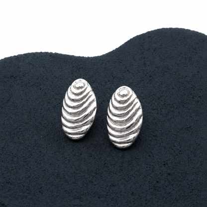 Silver shell-shaped earrings on a dark textured surface