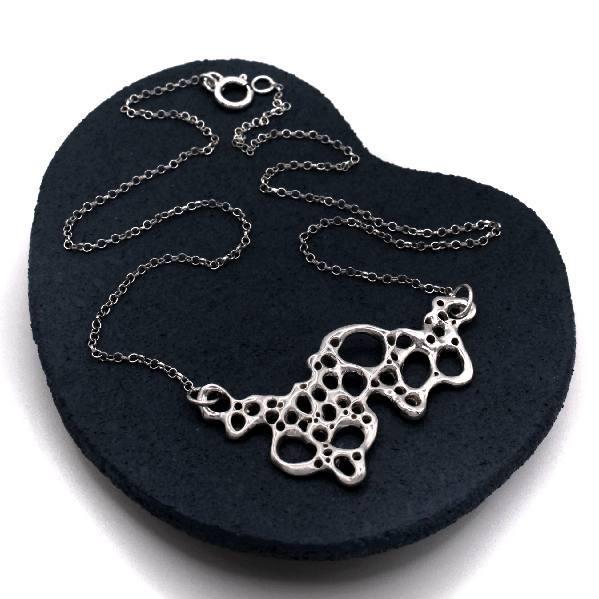 Silver necklace with a unique design on a black heart-shaped stand