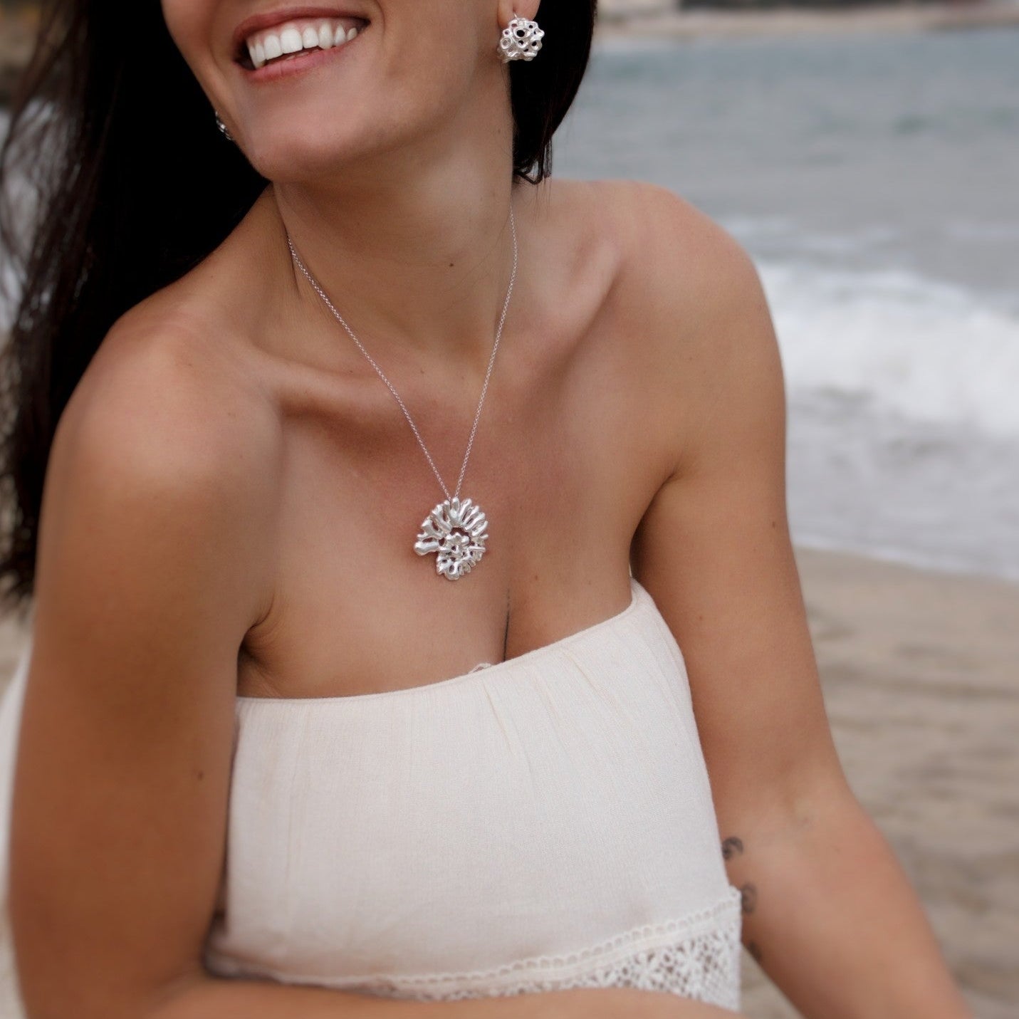 Woman wearing Souvenirs Espiral statement pendant in sterling silver on Mediterranean beach