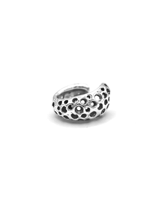 Piedra Poro sterling silver ear cuff with sculptural openwork inspired by porous Mediterranean stones on a white background.