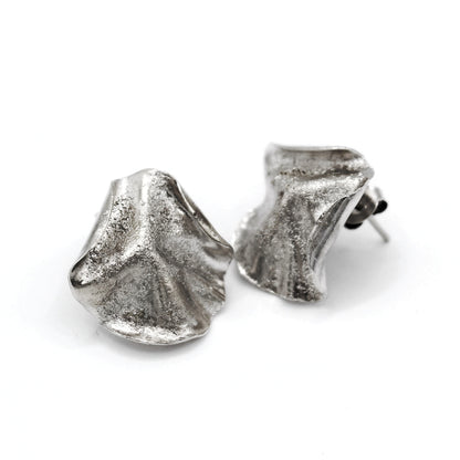 Sculptural folded silver earrings, handcrafted in recycled sterling silver using the lost wax casting technique. Mediterranean inspired jewelry with organic, wave like forms and a unique fused silver dust texture. Elegant and sustainable statement earrings for nature and contemporary jewelry lovers from Naturalesa. 