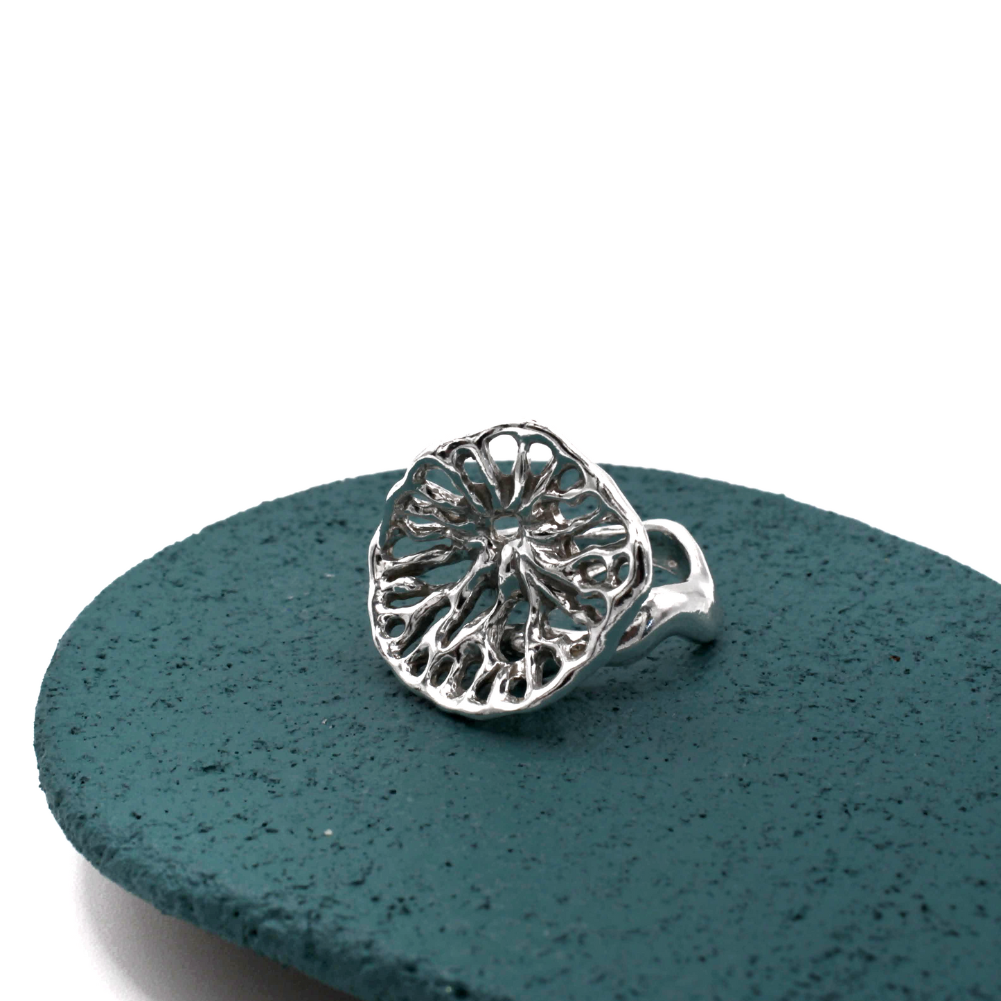 Silver ring with intricate design on a textured teal surface